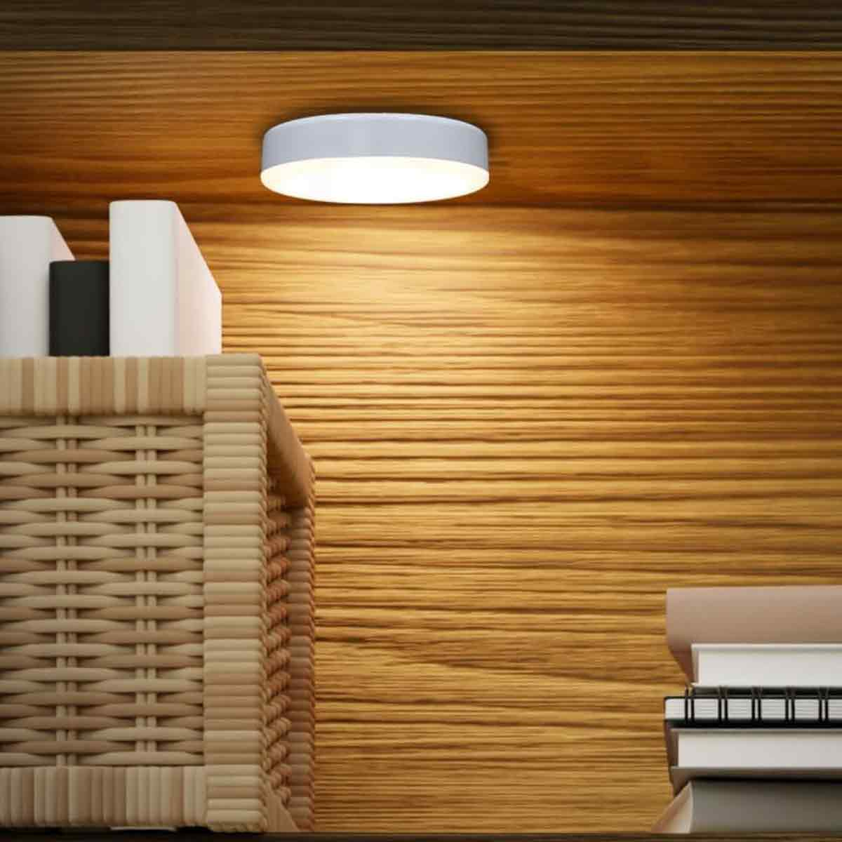 Ein weißes Licht beleuchtet ein Holzregal. Ein Weidenkorb und Bücher stehen auf dem Regal. Der Hintergrund ist eine Holztafel.