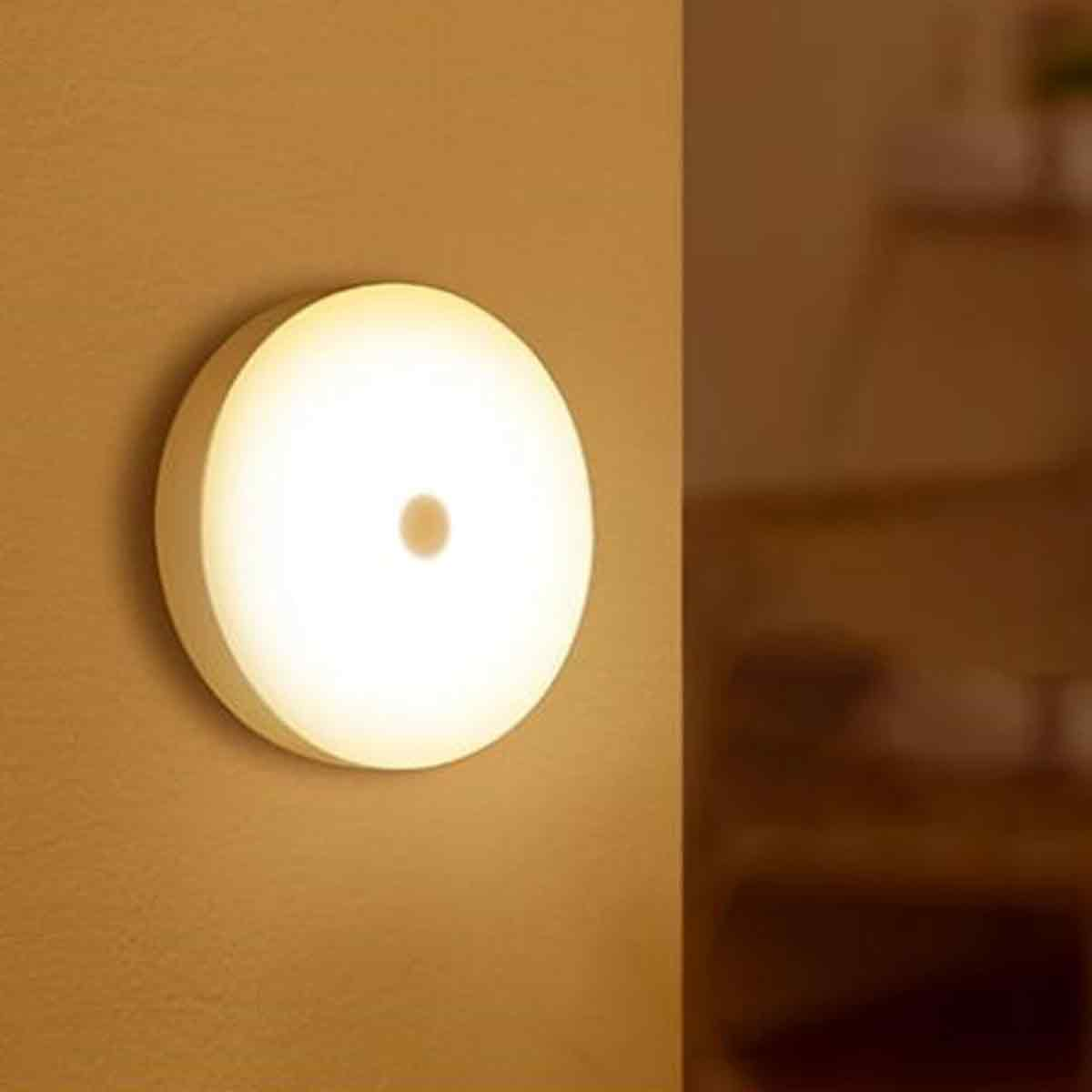Ein rundes, leuchtendes Wandlicht ist an einer braunen Wand befestigt. Es hat einen kleinen, braunen Mittelpunkt. Der Hintergrund zeigt einen verschwommenen Schrank.