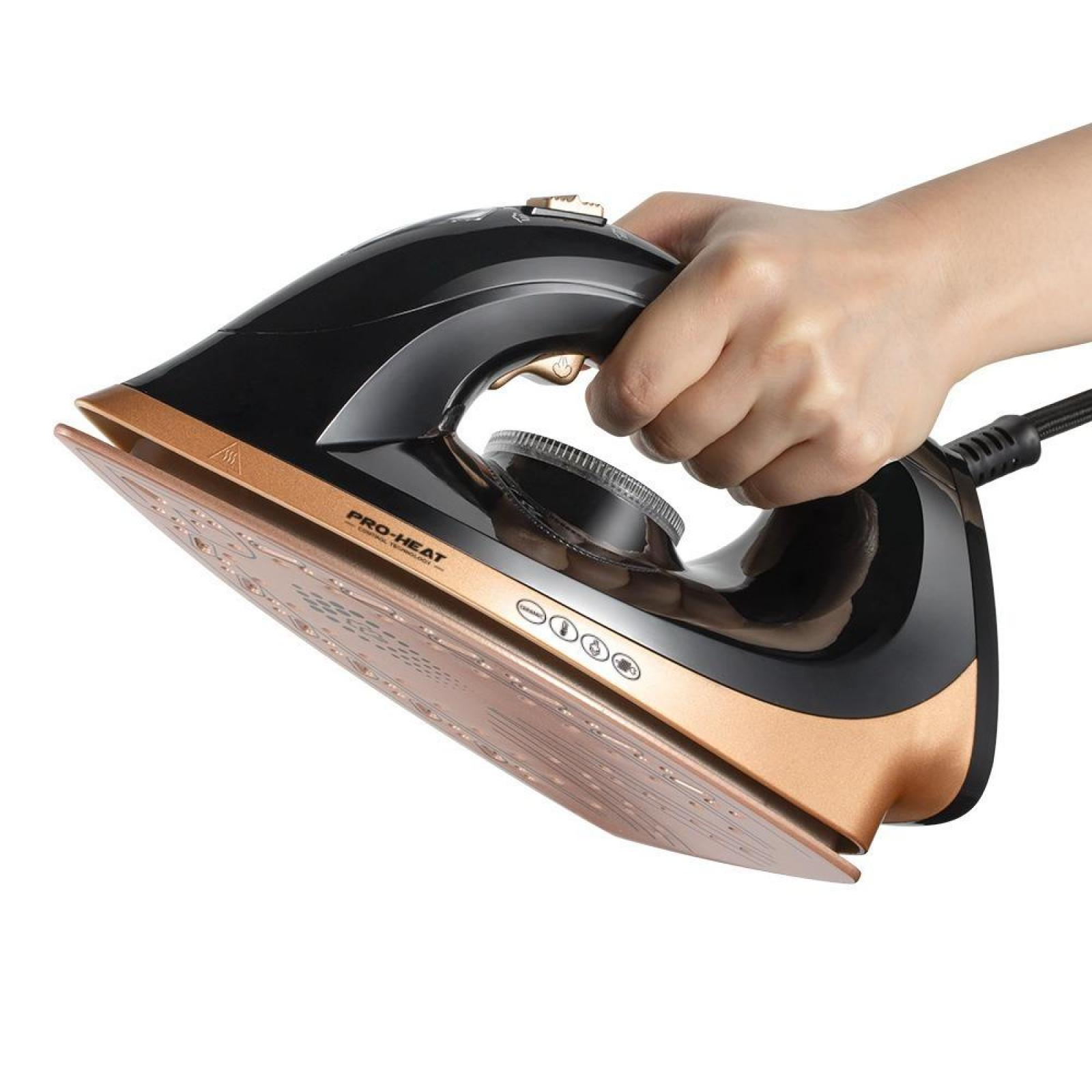 Eine Hand hält ein schwarzes und goldenes Bügeleisen, das mit einem Kabel verbunden ist. Die Basis des Bügeleisens ist hellbraun.