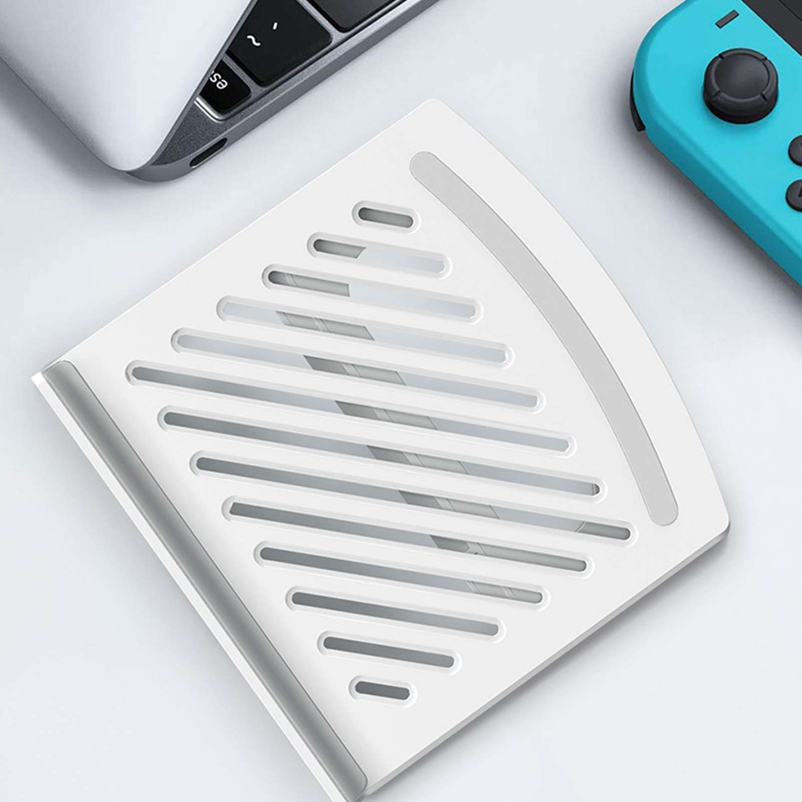 Ein weißes Eckregal mit Schlitzen, ein Laptop und ein türkisfarbener Gamecontroller auf einer weißen Oberfläche.