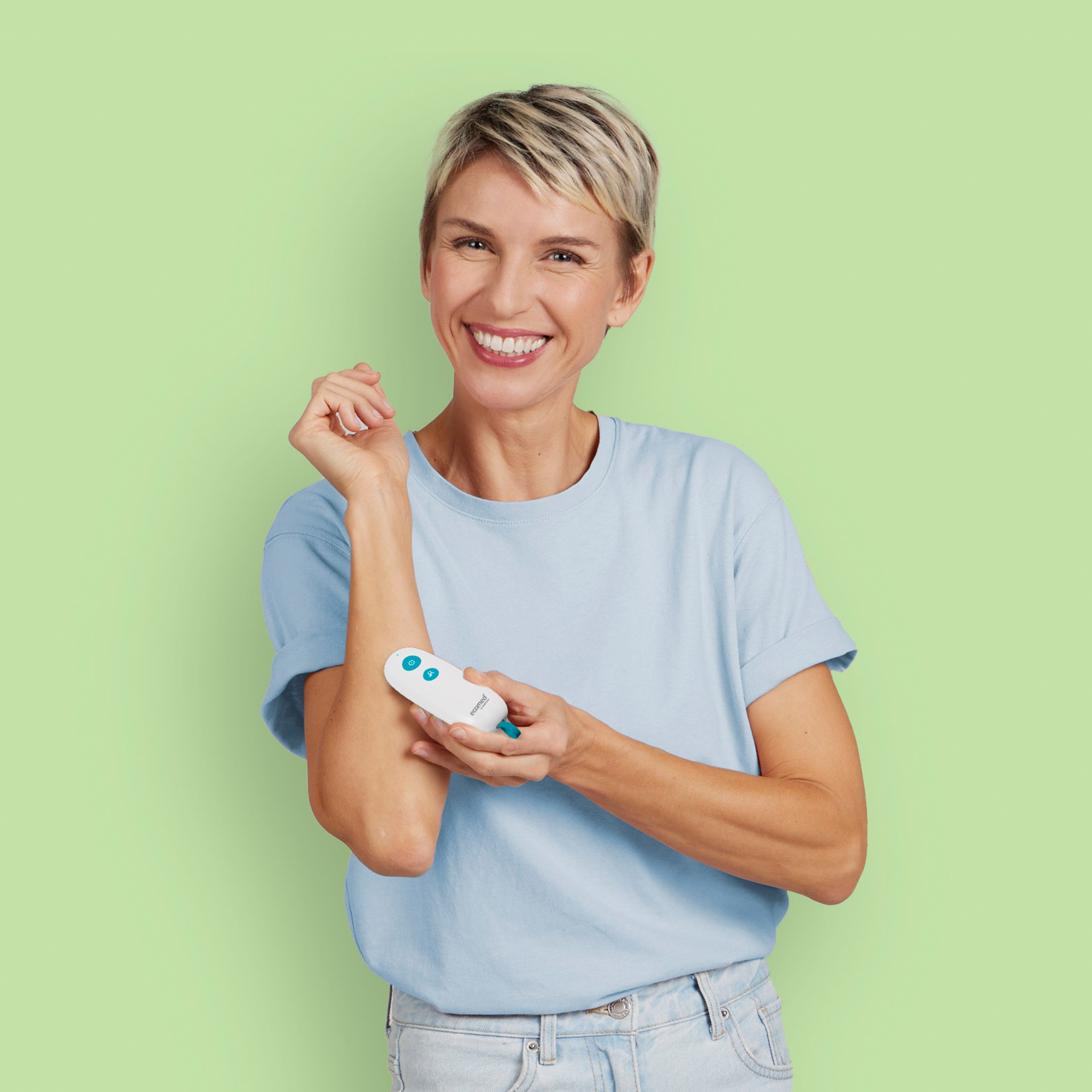 Een lachende vrouw houdt een wit medisch apparaat tegen haar arm. De achtergrond is lichtgroen.