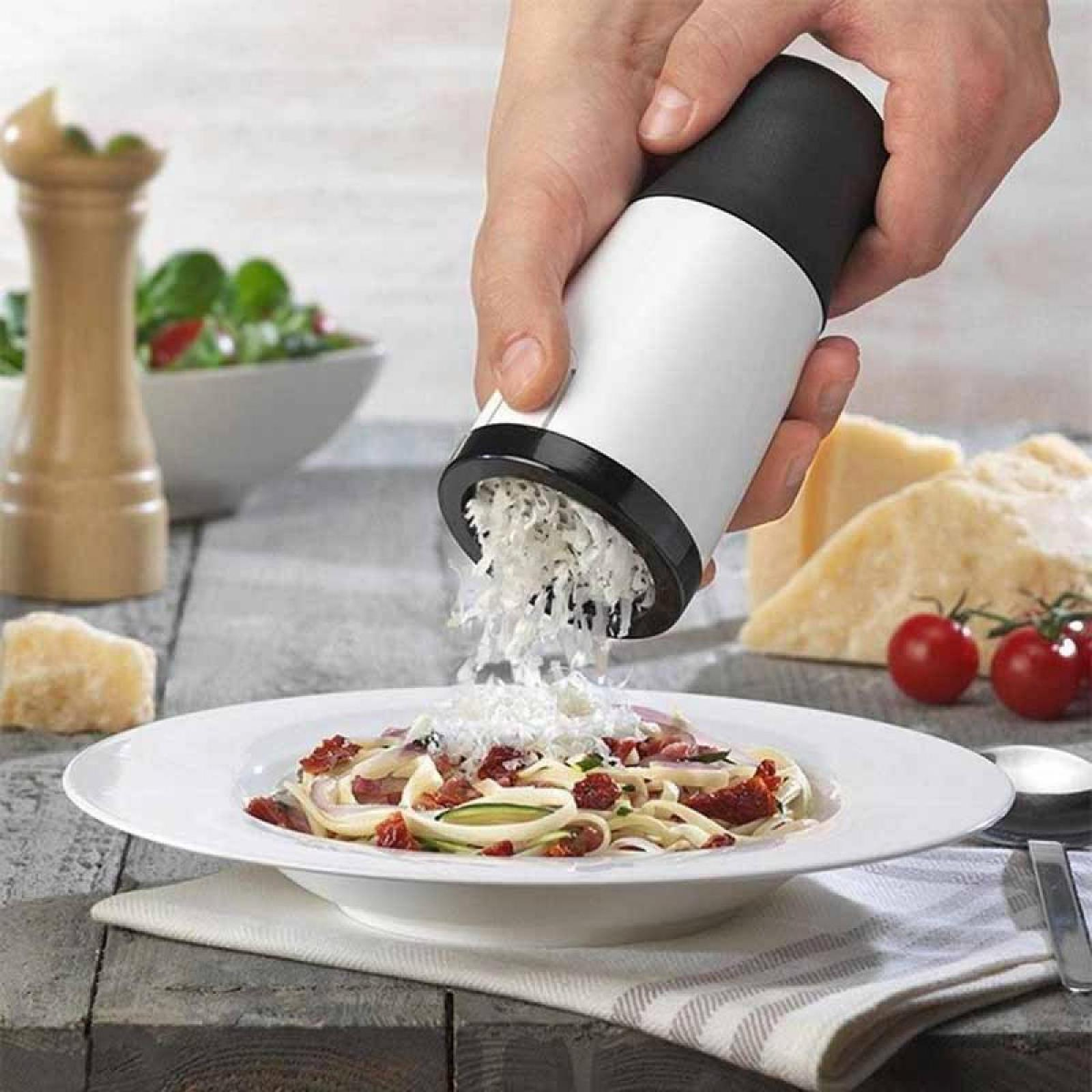 Eine Hand reibt Käse über Pasta. Im Hintergrund befinden sich ein hölzerner Pfefferstreuer und Tomaten.