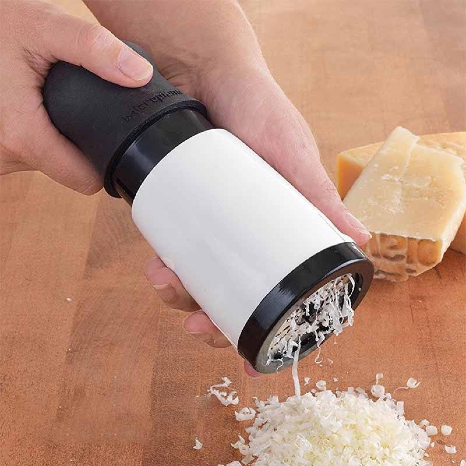 Eine Hand reibt Käse mit einer Reibe. Geriebener Käse fällt auf eine Holzoberfläche. Käsescheiben sind im Hintergrund.