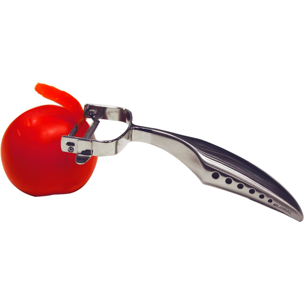 Ein Metallschäler schält eine rote Tomate. Ein Streifen Tomatenschale rollt sich ab. Weißer Hintergrund.