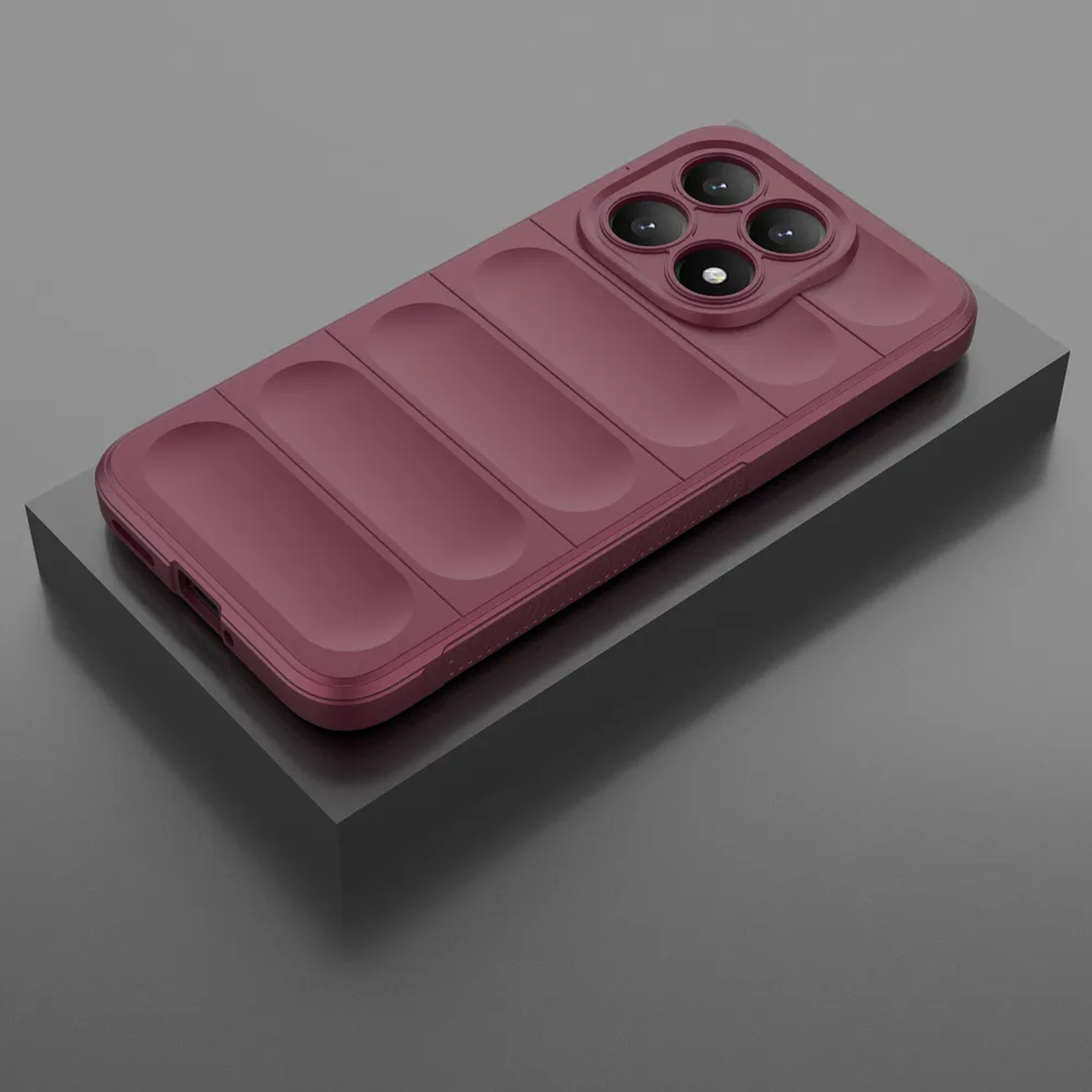 Een bordeauxrode telefoonhoes met vier cameralenzen ligt op een zwart blok tegen een grijze achtergrond.