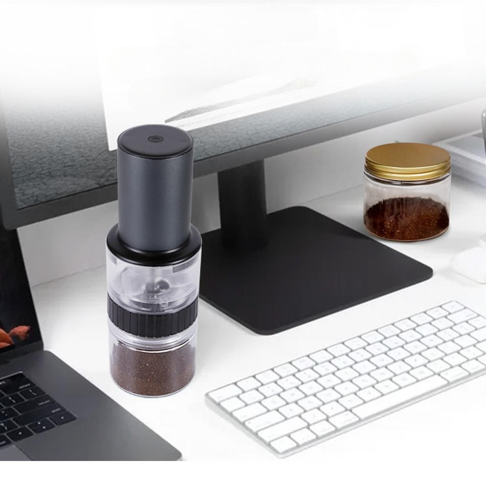 Eine Kaffeemühle steht auf einem Schreibtisch mit einer Tastatur, einem Laptop und einem Glas Kaffee. Im Hintergrund befindet sich ein Monitor.