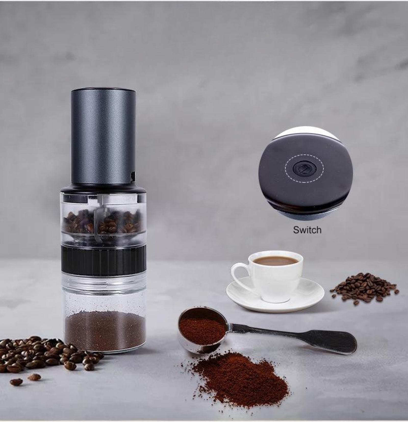 Eine Kaffeemühle mit Kaffeebohnen, gemahlenem Kaffee, einer Tasse Kaffee und einem Messlöffel auf grauer Oberfläche.