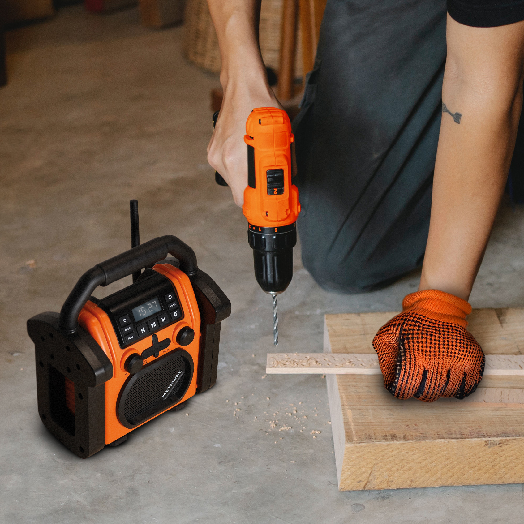 Una persona taladra madera con un taladro naranja. A la izquierda hay una radio naranja. La persona usa guantes.
