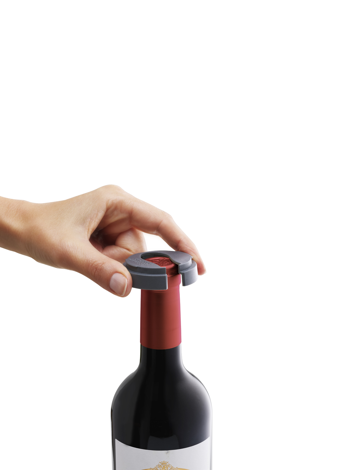 Una mano coloca un abridor de vino gris sobre una botella de vino con la parte superior roja. La botella es negra con etiqueta blanca.