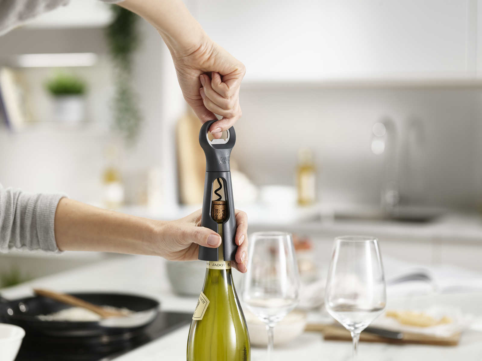 Una persona usa un sacacorchos para abrir una botella de vino. Dos copas de vino sobre la mesa, fondo de cocina.