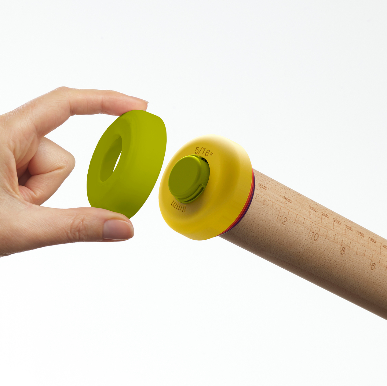 Una mano sostiene un anillo verde cerca del extremo amarillo de un rodillo. El extremo tiene un botón verde y la etiqueta 5/16". El rodillo es de madera.