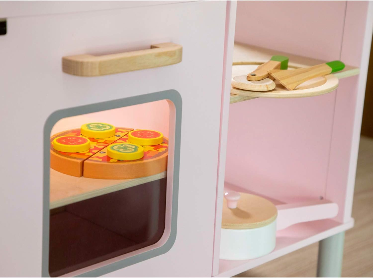 Eine rosa Spielzeugküche mit Pizza im Ofen und Kochutensilien. Die Pizza hat gelbe und rote Beläge.