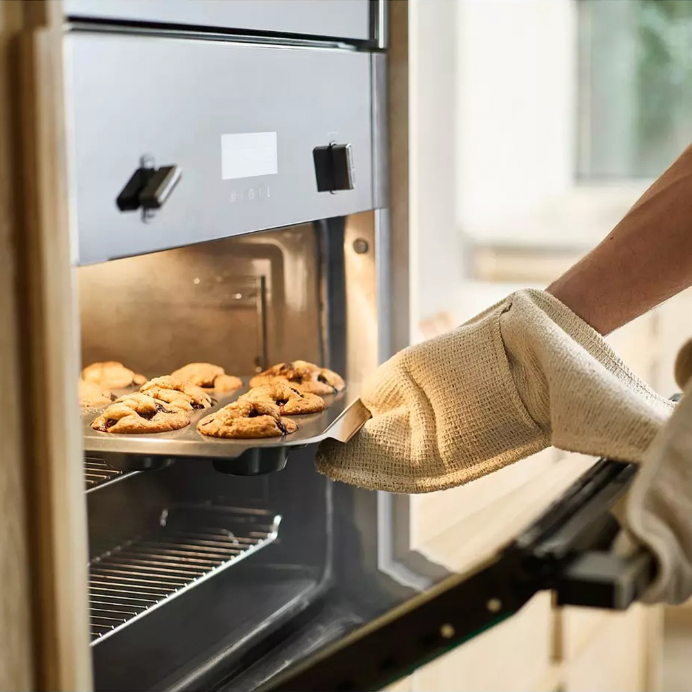 Eine Person mit Ofenhandschuh nimmt ein Blech mit gebackenen Keksen aus dem Ofen. Die Kekse sind goldbraun.