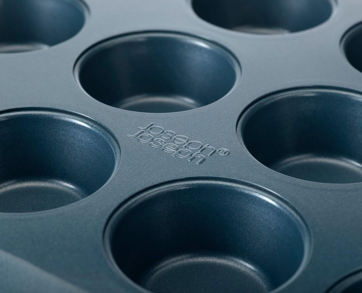 Nahaufnahme einer tealfarbenen Muffinform. Die kreisförmigen Formen sind leer. Das Joseph Joseph Logo ist sichtbar.