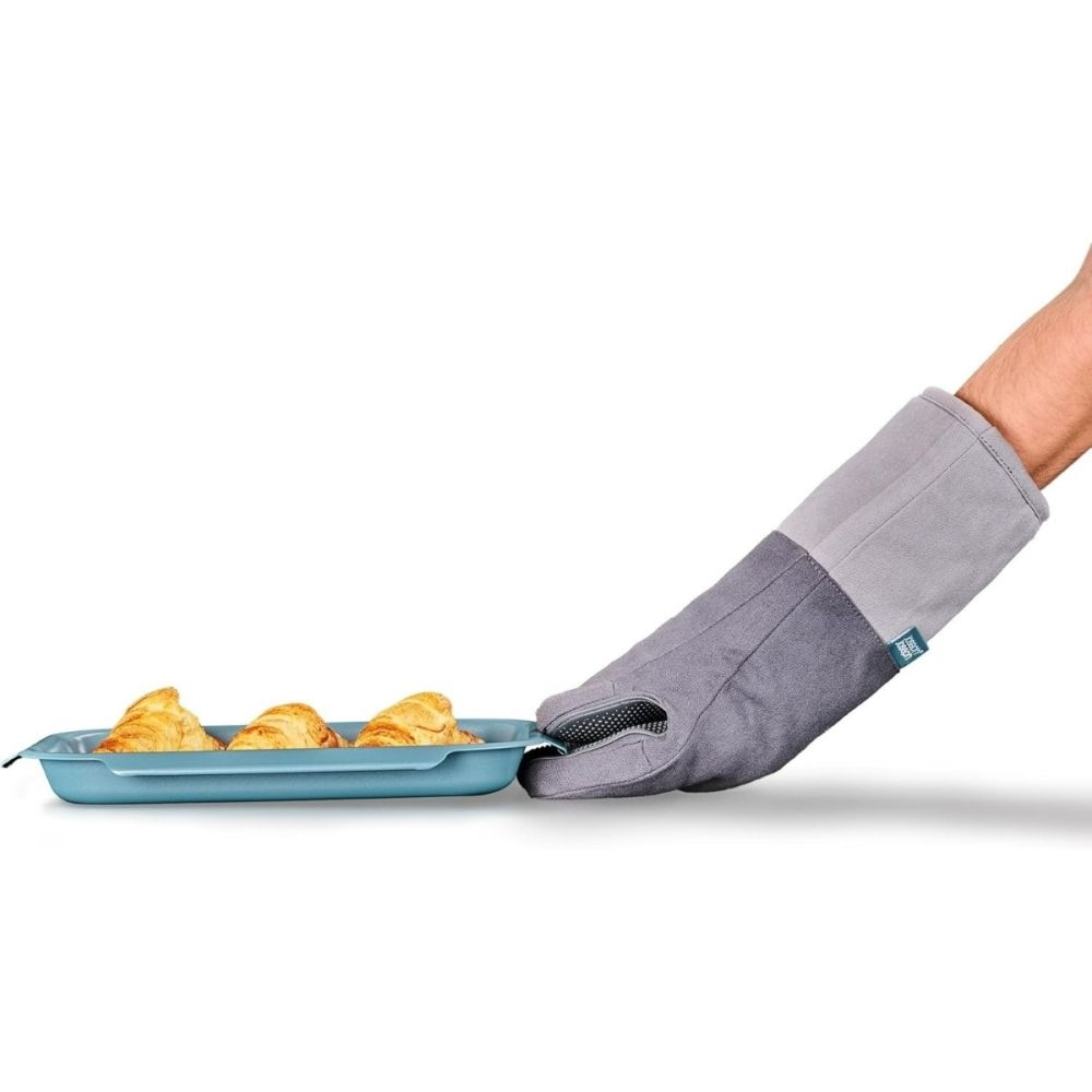 Eine Hand mit einem grauen Ofenhandschuh hält eine blaue Backform mit drei Croissants. Weißer Hintergrund.