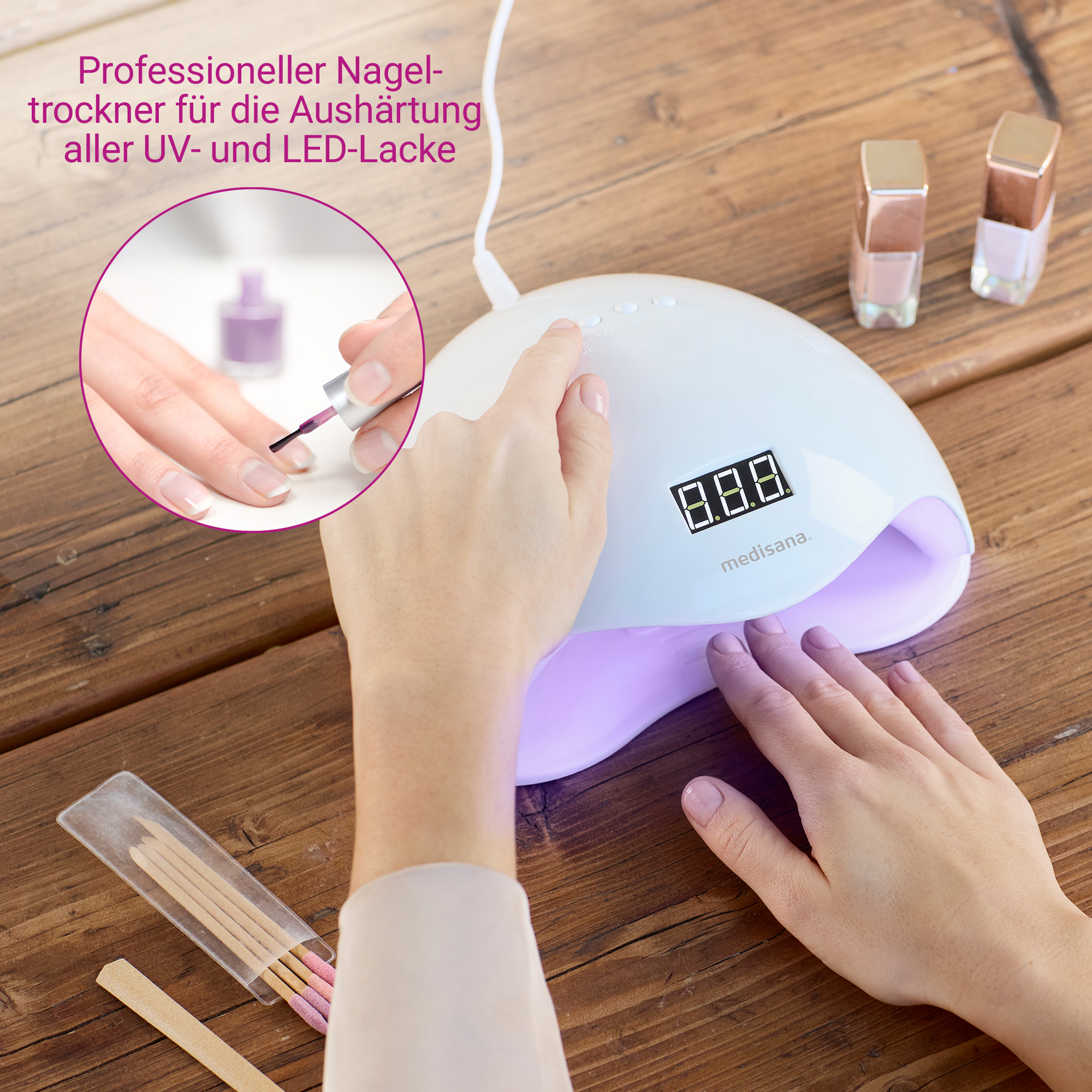 Ein Nageltrockner mit einer Hand darin, ein bemalter Nagel, Nagellackflaschen und Nagelwerkzeuge auf einem Holztisch.