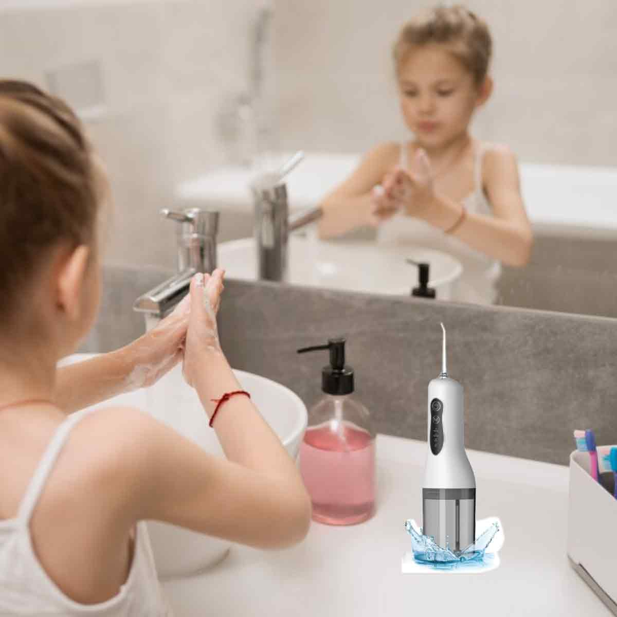 Zwei Mädchen waschen sich im Badezimmer die Hände. Auf dem Tresen sind Seife, ein Wasserflosser und ein Spiegel.