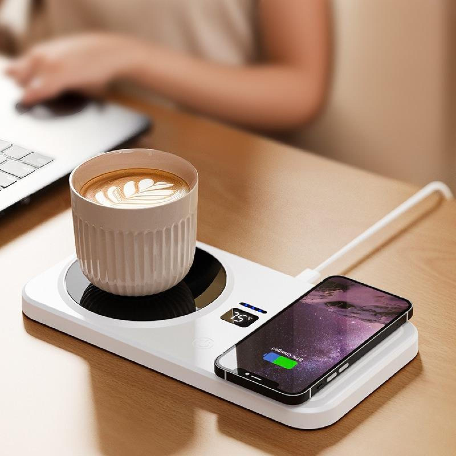 Eine Kaffeetasse auf einer Heizauflage, Telefon wird geladen. Im unscharfen Hintergrund arbeitet eine Person an einem Laptop.