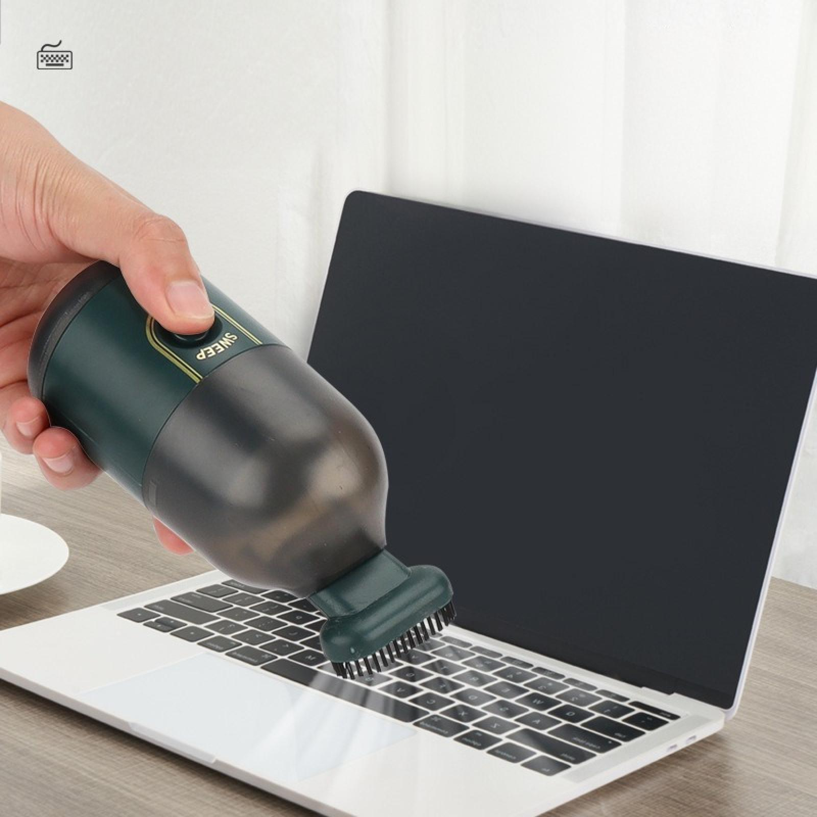 Eine Hand benutzt einen Mini-Staubsauger auf einer Laptop-Tastatur. Der Staubsauger ist dunkelgrün und schwarz.
