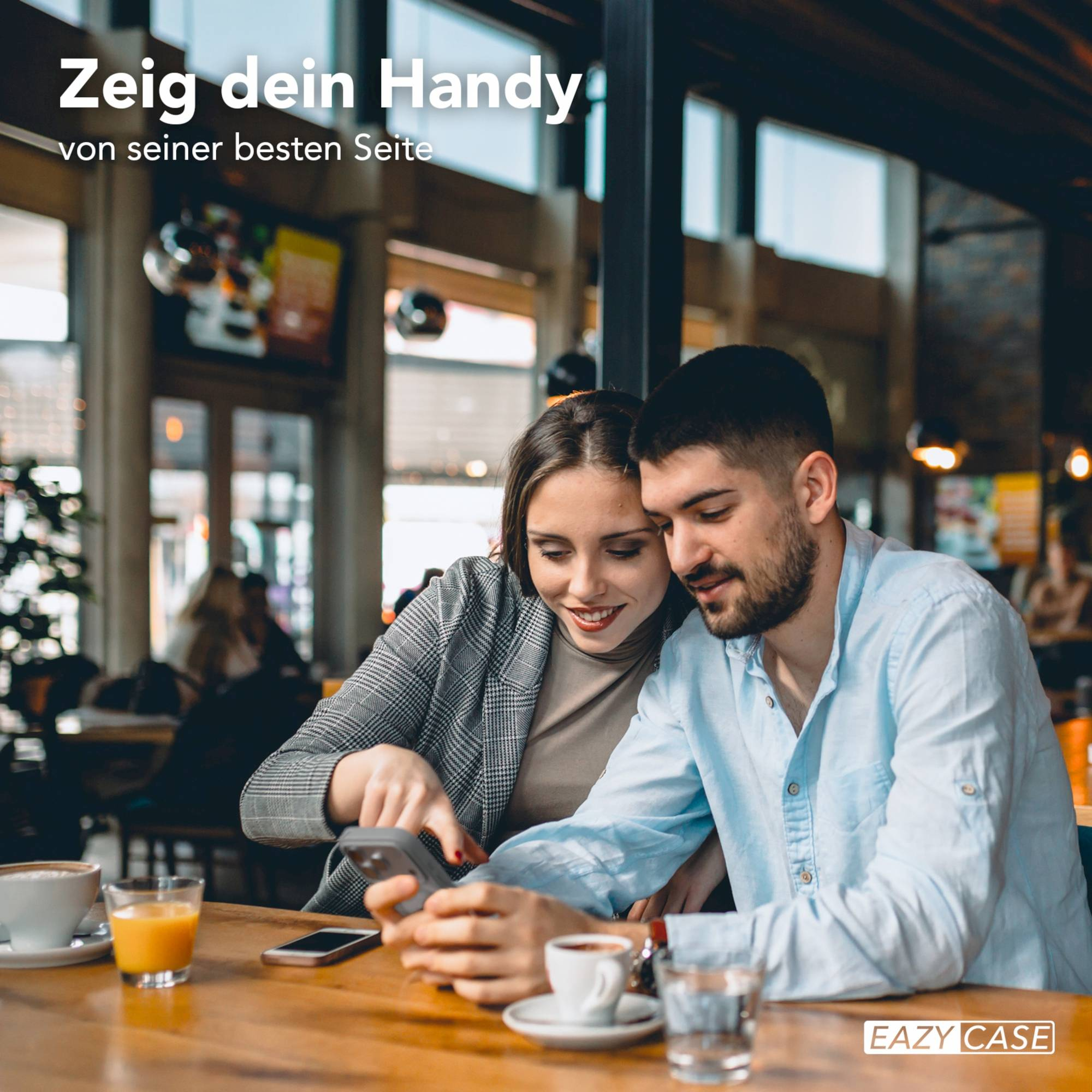 Ein Paar betrachtet in einem Café ein Telefon. Getränke und ein Telefon stehen auf dem Tisch. Der Mann trägt ein blaues Hemd.