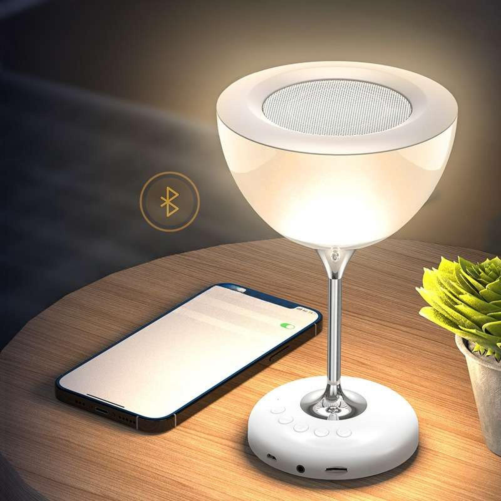 Eine weiße Lampe in Form eines Weinglases. Ein Telefon und eine Pflanze stehen auf dem Holztisch.