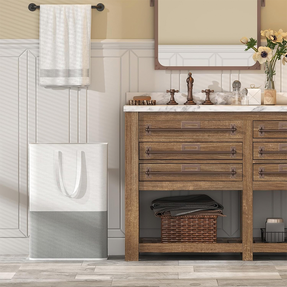 Baño con tocador de madera, espejo y cesto de ropa sucia. Cuelga una toalla y hay flores encima del tocador.
