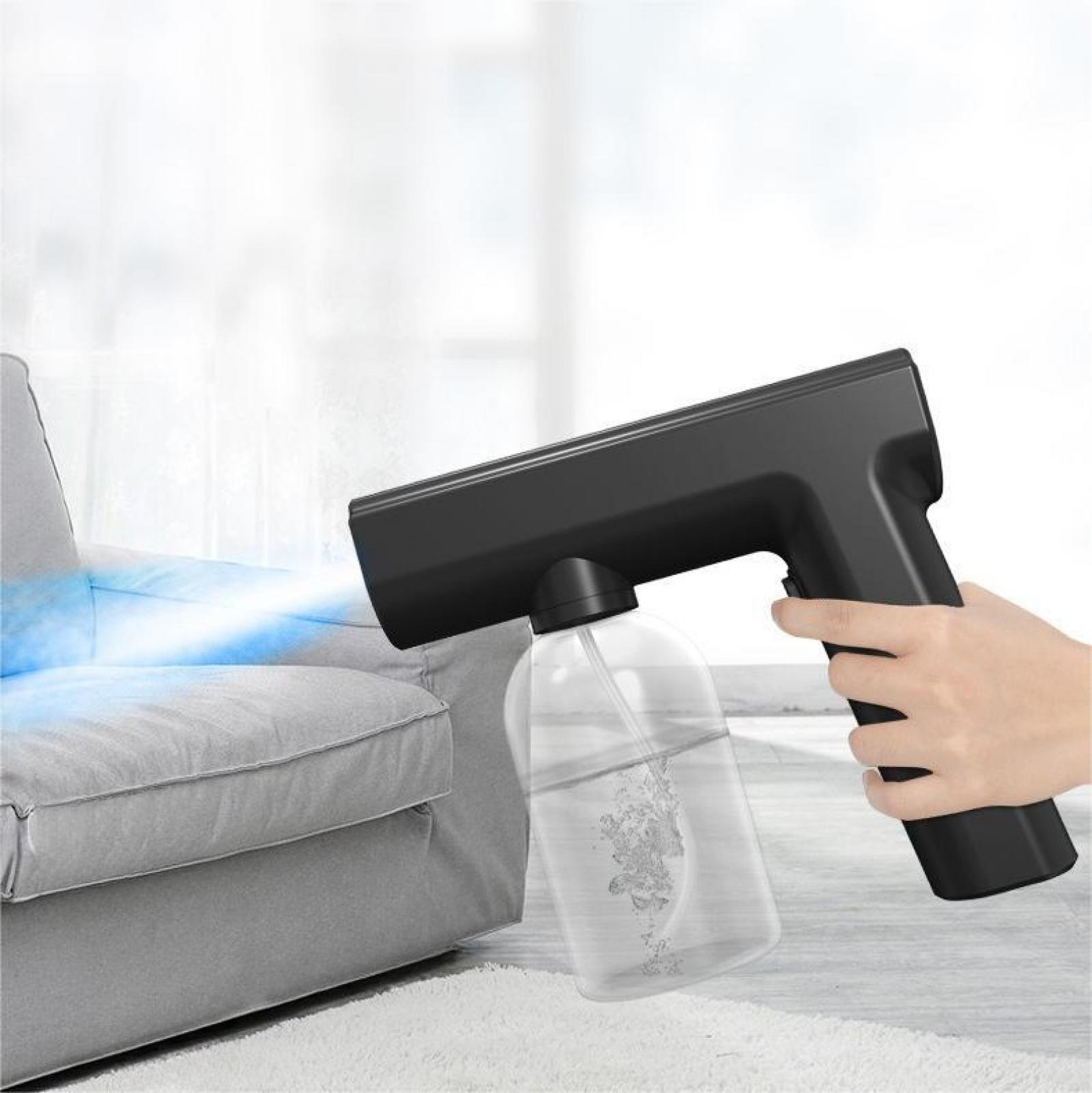 Eine Hand hält ein schwarzes Desinfektionssprühgerät. Es sprüht einen blauen Nebel auf ein graues Sofa.