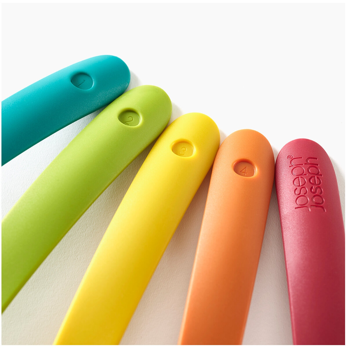 Primer plano de cinco utensilios de cocina coloridos: verde azulado, verde, amarillo, naranja y rojo. Cada uno tiene un número. El rojo tiene una marca.