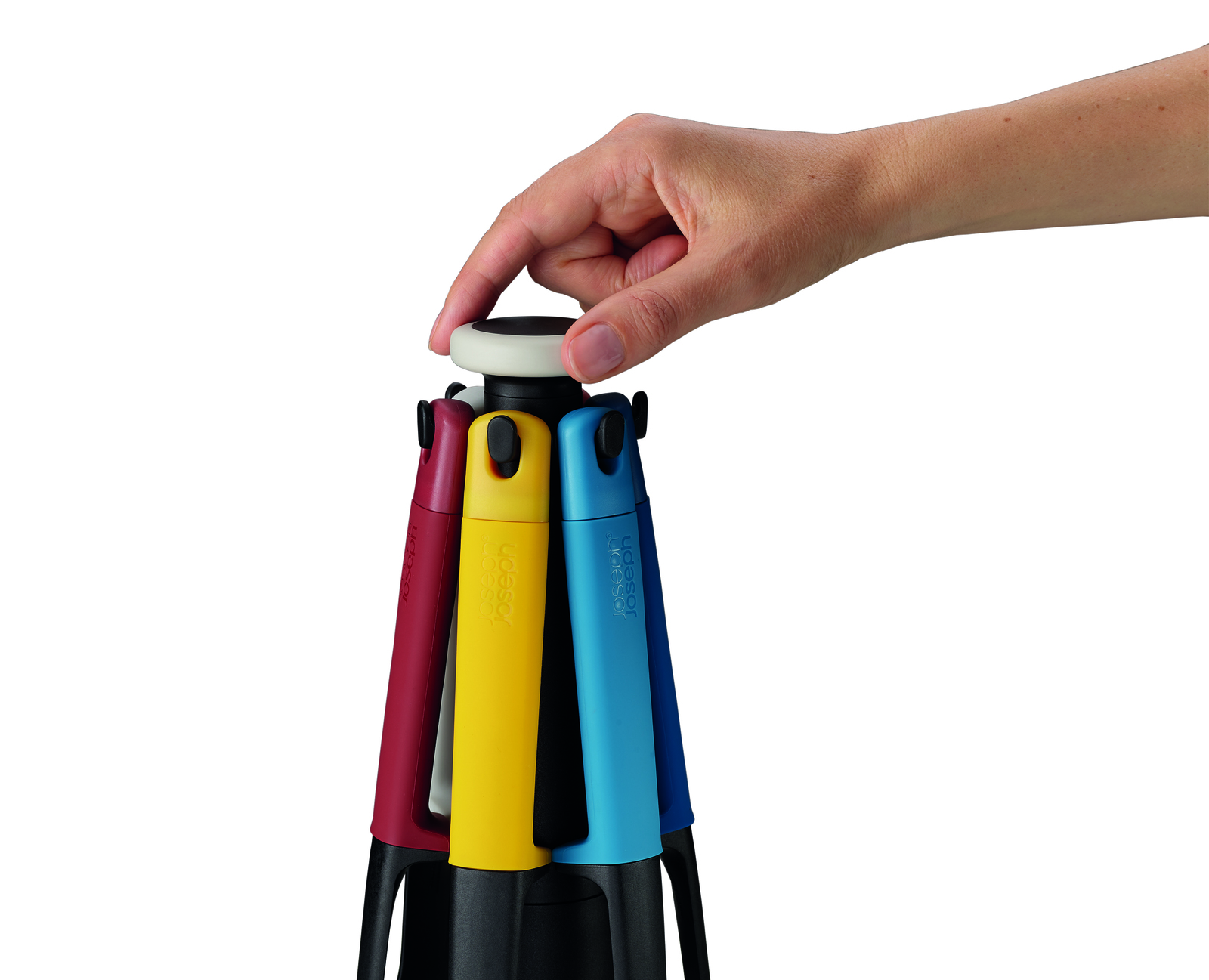 Una mano presiona un botón blanco en un utensilio de cocina multicolor. Los colores incluyen rojo, amarillo y azul. Fondo blanco.