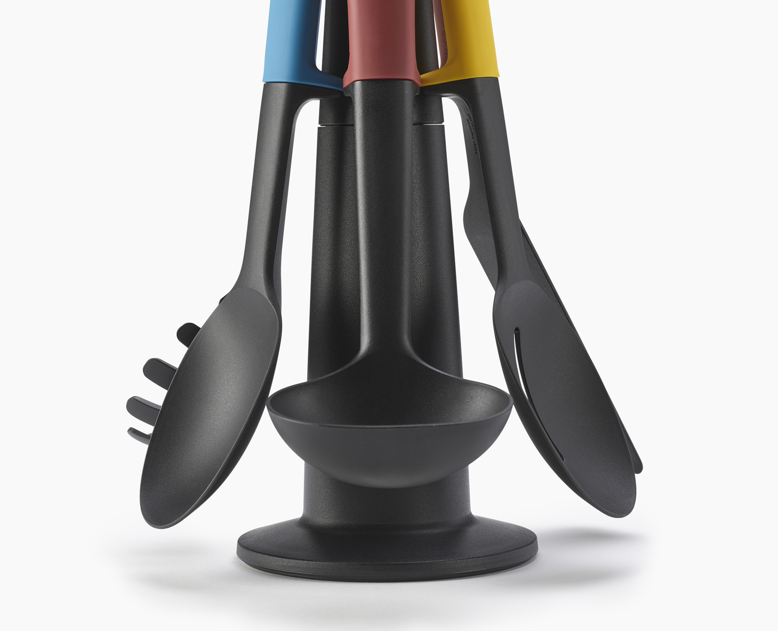 Un juego de utensilios de cocina negros con mangos de colores (azul, rojo, amarillo) en un soporte negro, aislado sobre blanco.