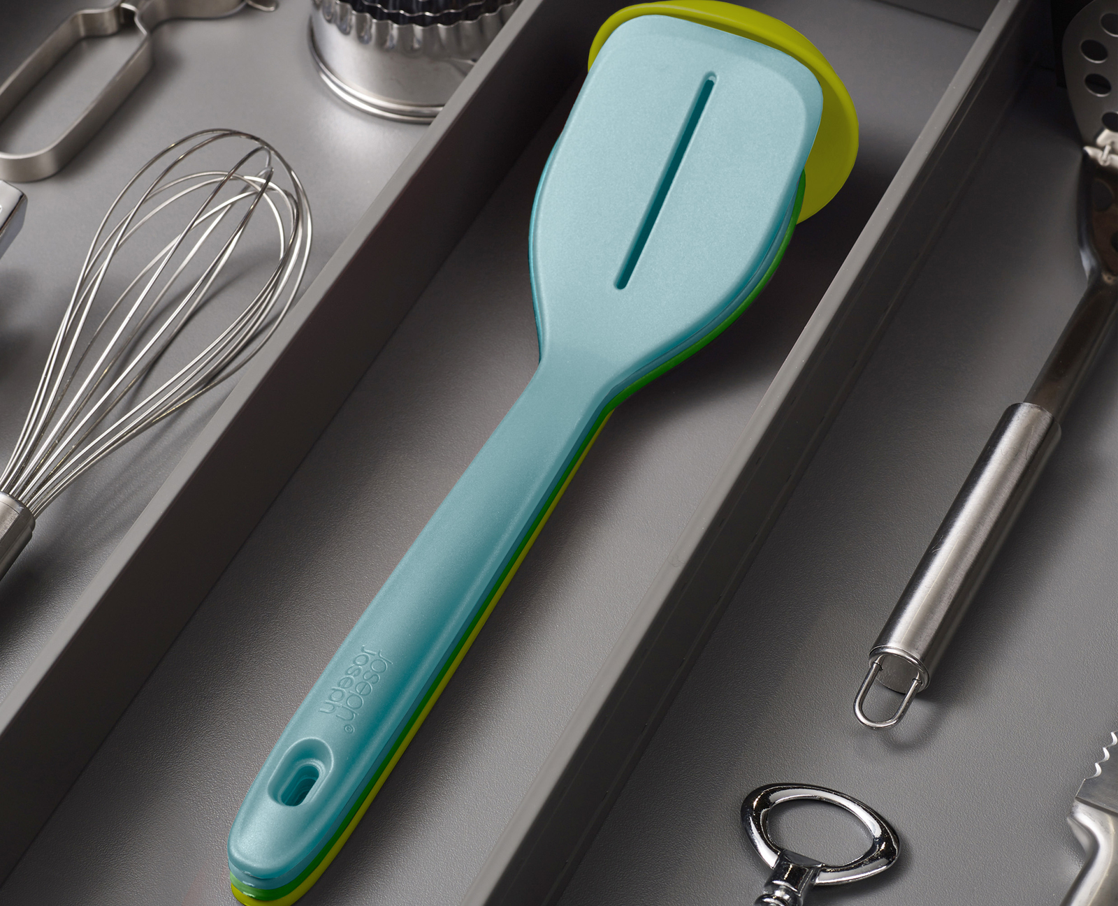 Primer plano de utensilios de cocina en un cajón. Una espátula azul está enfocada, con otras herramientas como batidores y abridores de botellas.