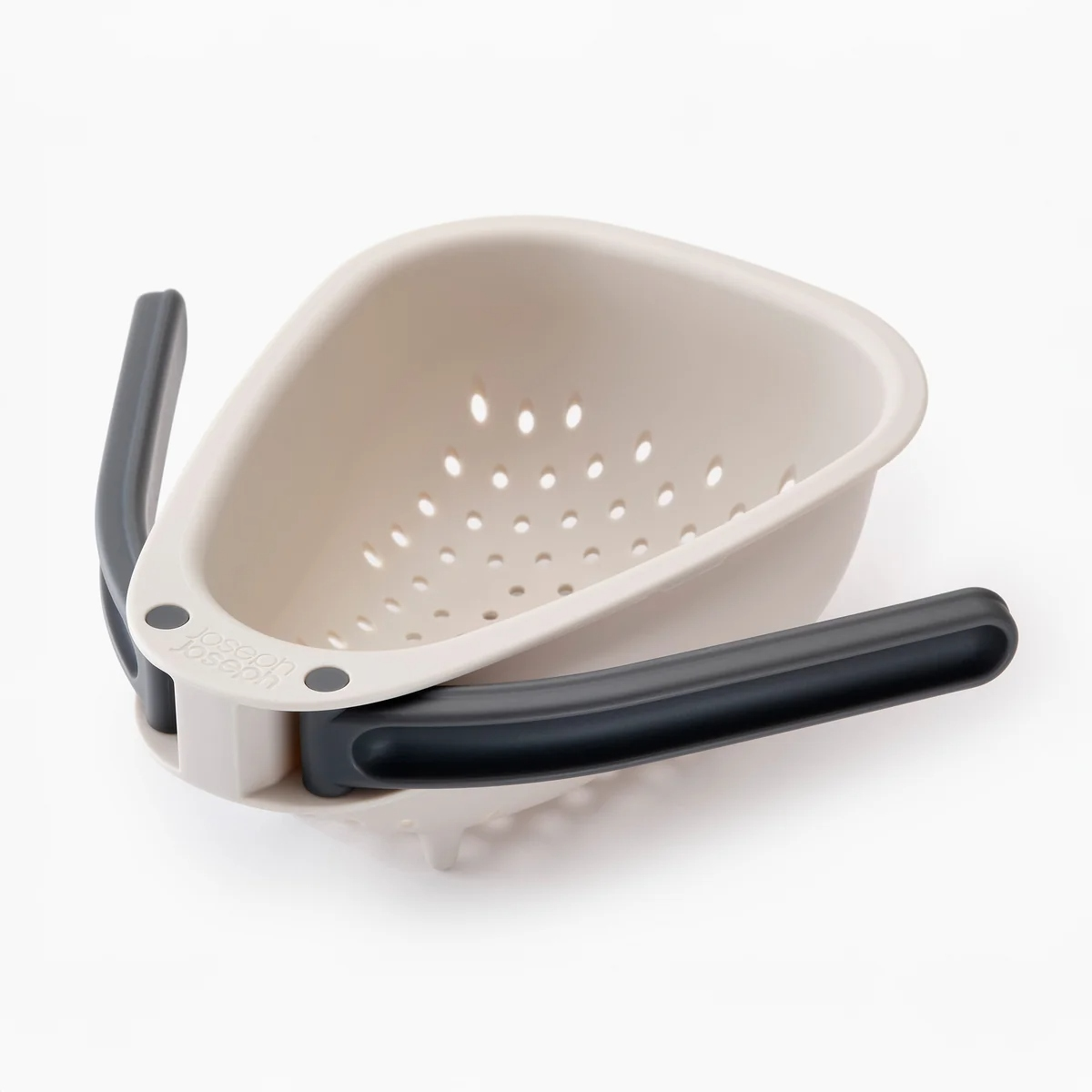 Scolapasta triangolare color crema con manici e fori grigio scuro. Si trova su una superficie bianca, il logo Joseph Joseph è visibile.