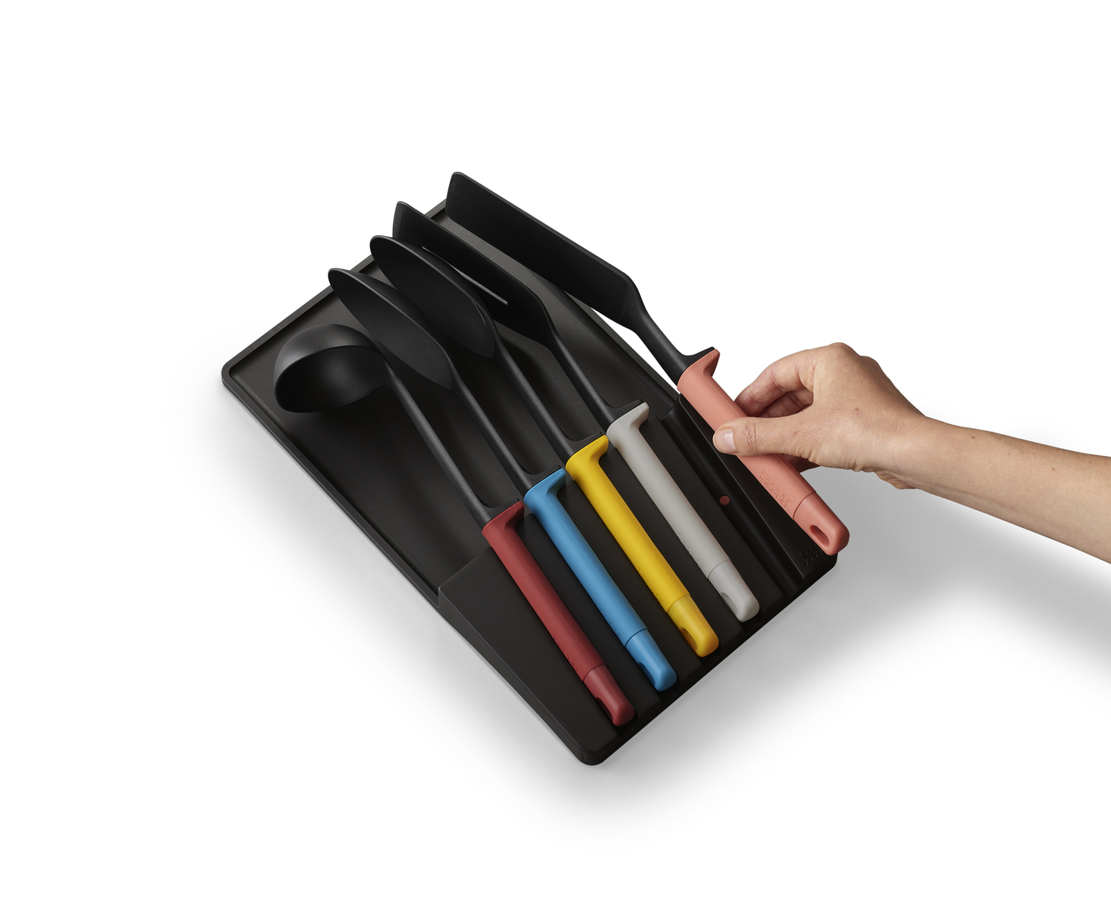 Utensilios de cocina negros con mangos coloridos en una bandeja negra. Una mano sostiene un utensilio rosa.