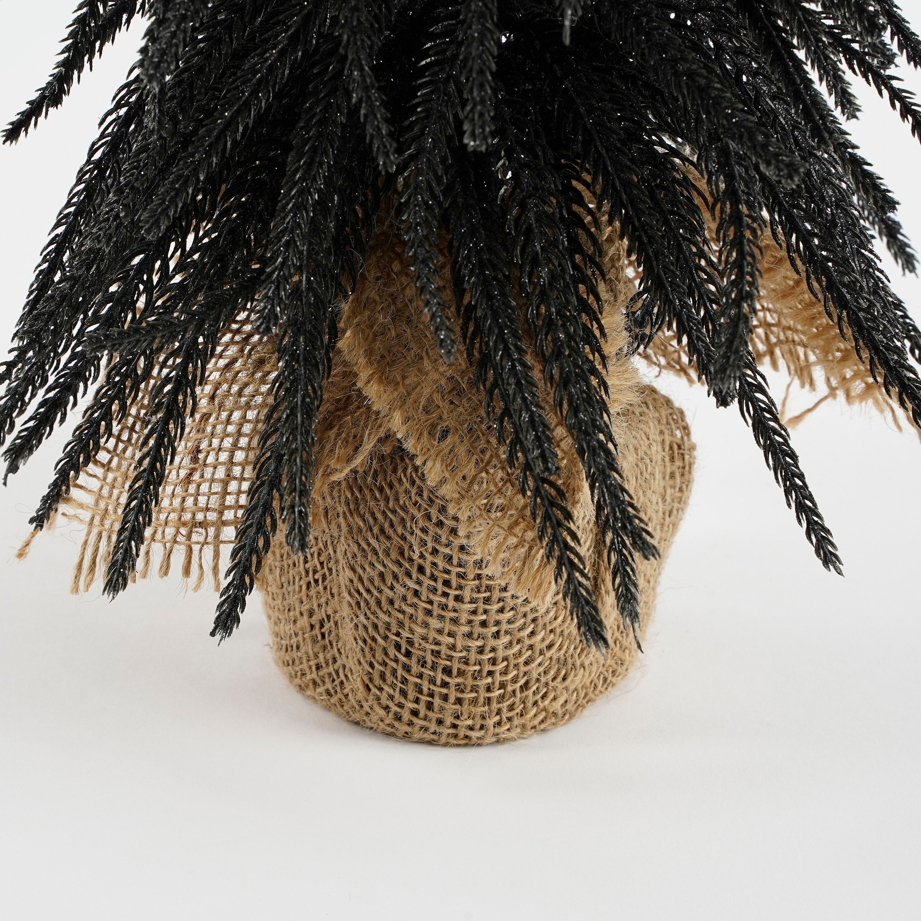 Sapin de Noël artificiel noir avec base en toile de jute sur fond blanc.
