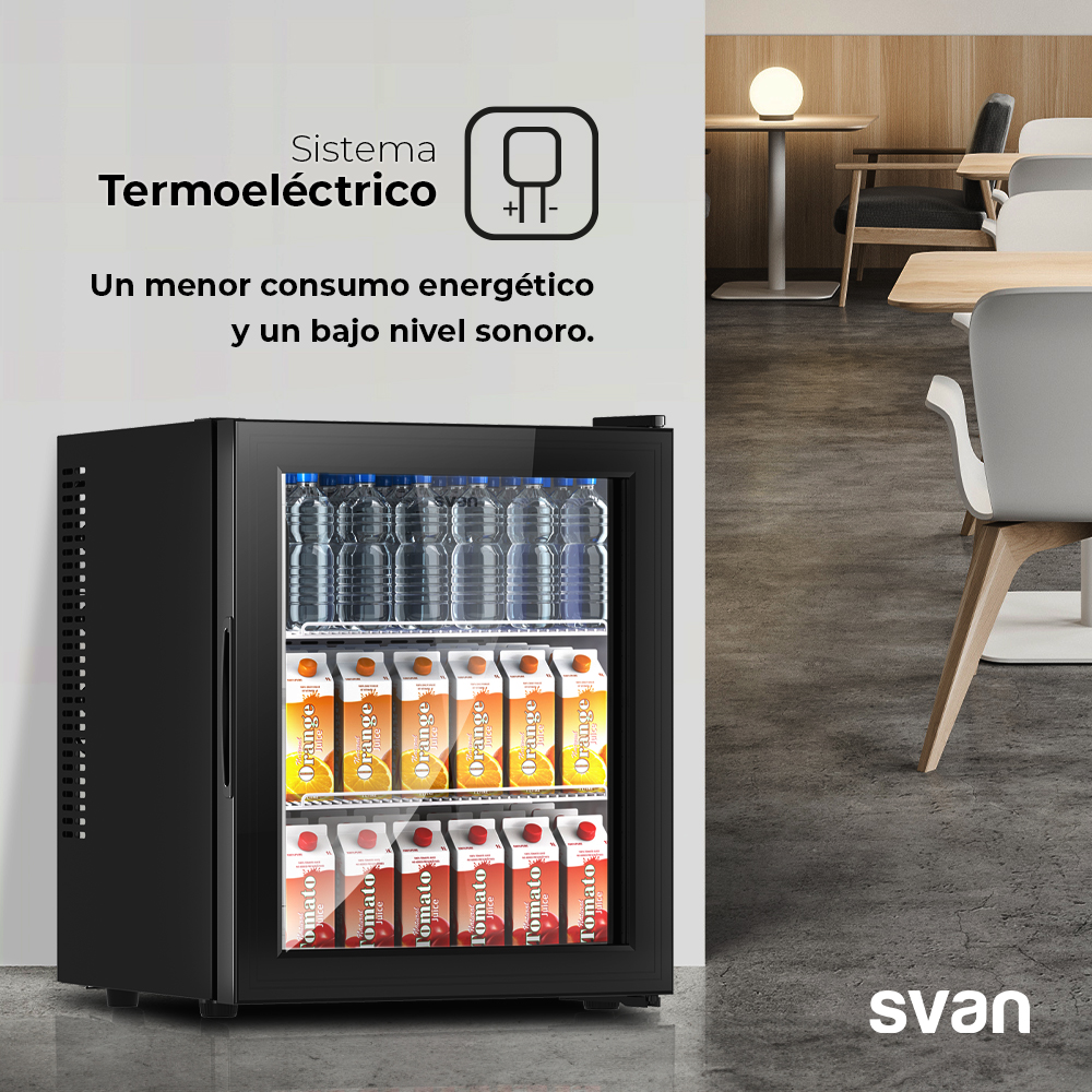 Mini-nevera negra con bebidas. Se ven cartones de zumo de naranja y tomate. Botellas de agua en la parte superior. Ambiente de restaurante.
