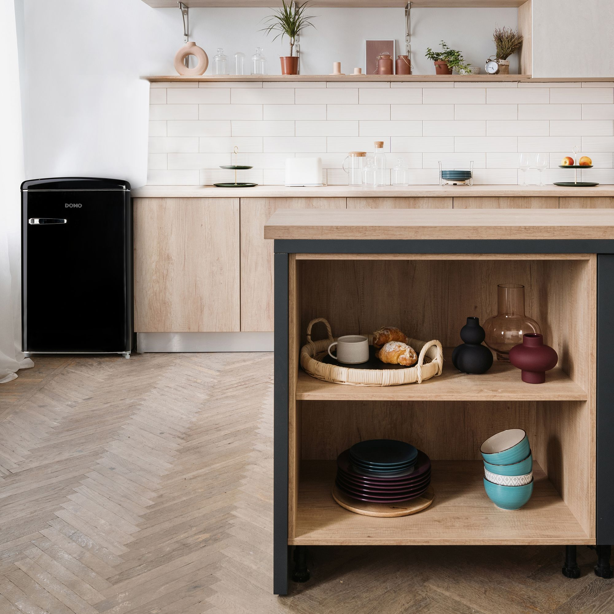 Cuisine avec réfrigérateur noir, étagères en bois et divers objets comme des bols, assiettes et vases.