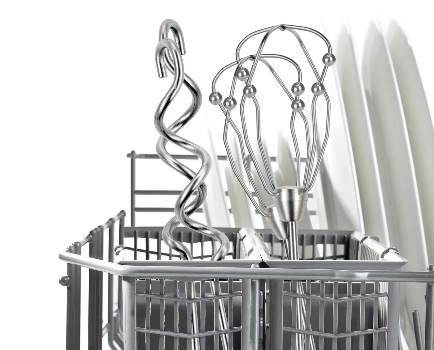 Wnętrze zmywarki z metalowymi przyborami: trzepaczką, mieszalnikiem spiralnym i talerzami. Szary stojak z przodu, białe tło.
