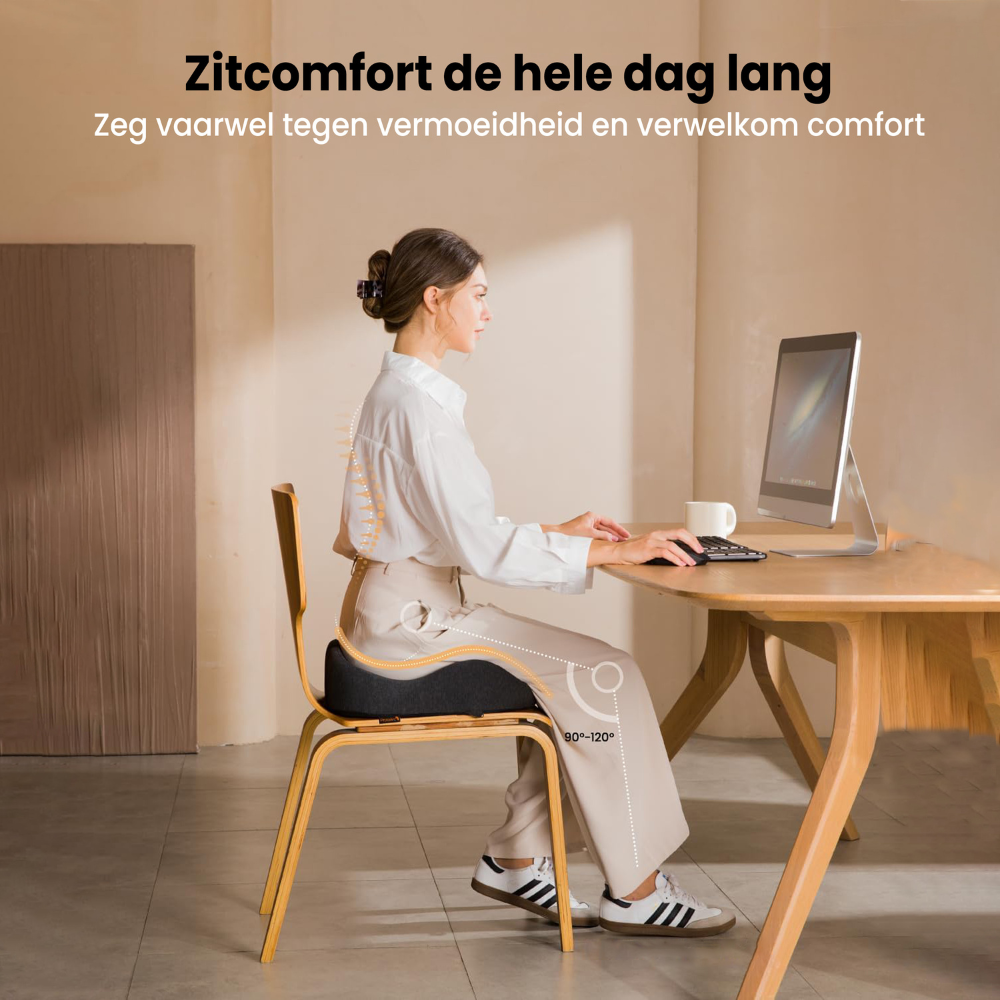 A woman sits at a desk, typing on a keyboard. She is using a cushion on the chair. The text says: Zitcomfort de hele dag lang.