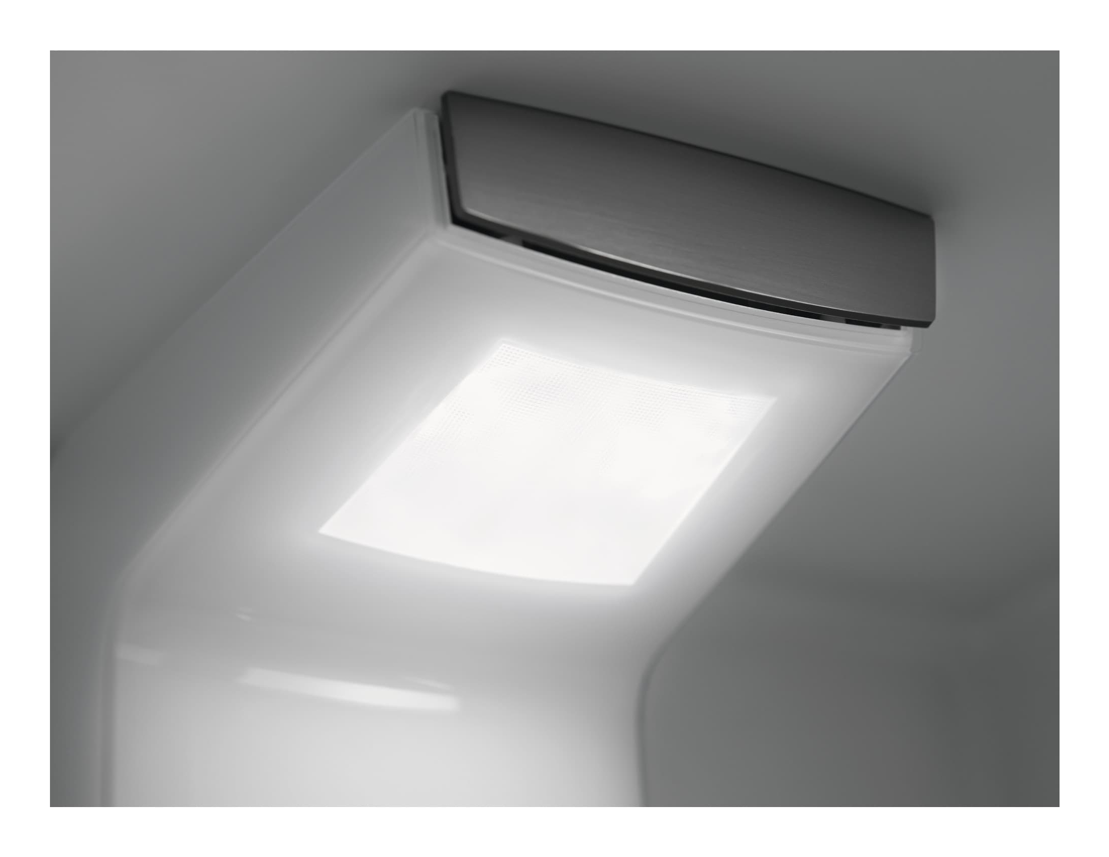 Close-up van een wit, gloeiend armatuur met een zilverkleurige metalen bovenkant, tegen een grijze achtergrond.