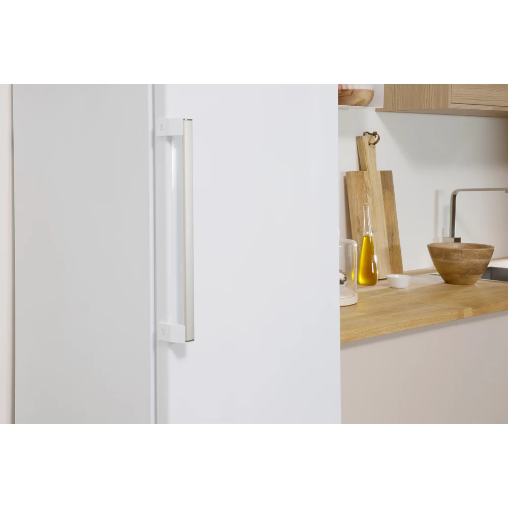 Puerta de refrigerador blanca con manija plateada. Encimera de cocina con aceite de oliva, tablas de cortar y un cuenco de madera.