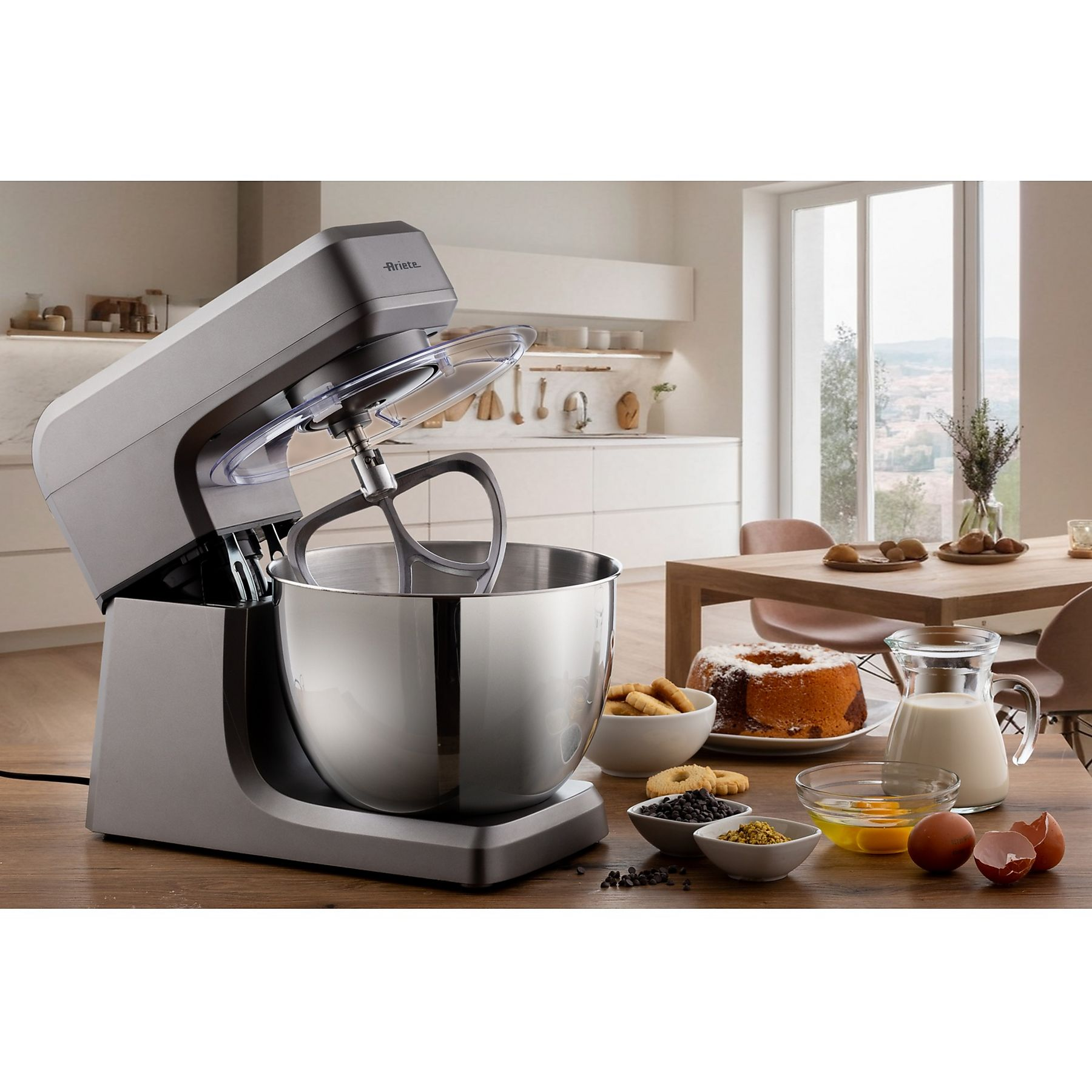 Un mixer da cucina con una ciotola è su un tavolo di legno. Anche torte e ingredienti sono sul tavolo.
