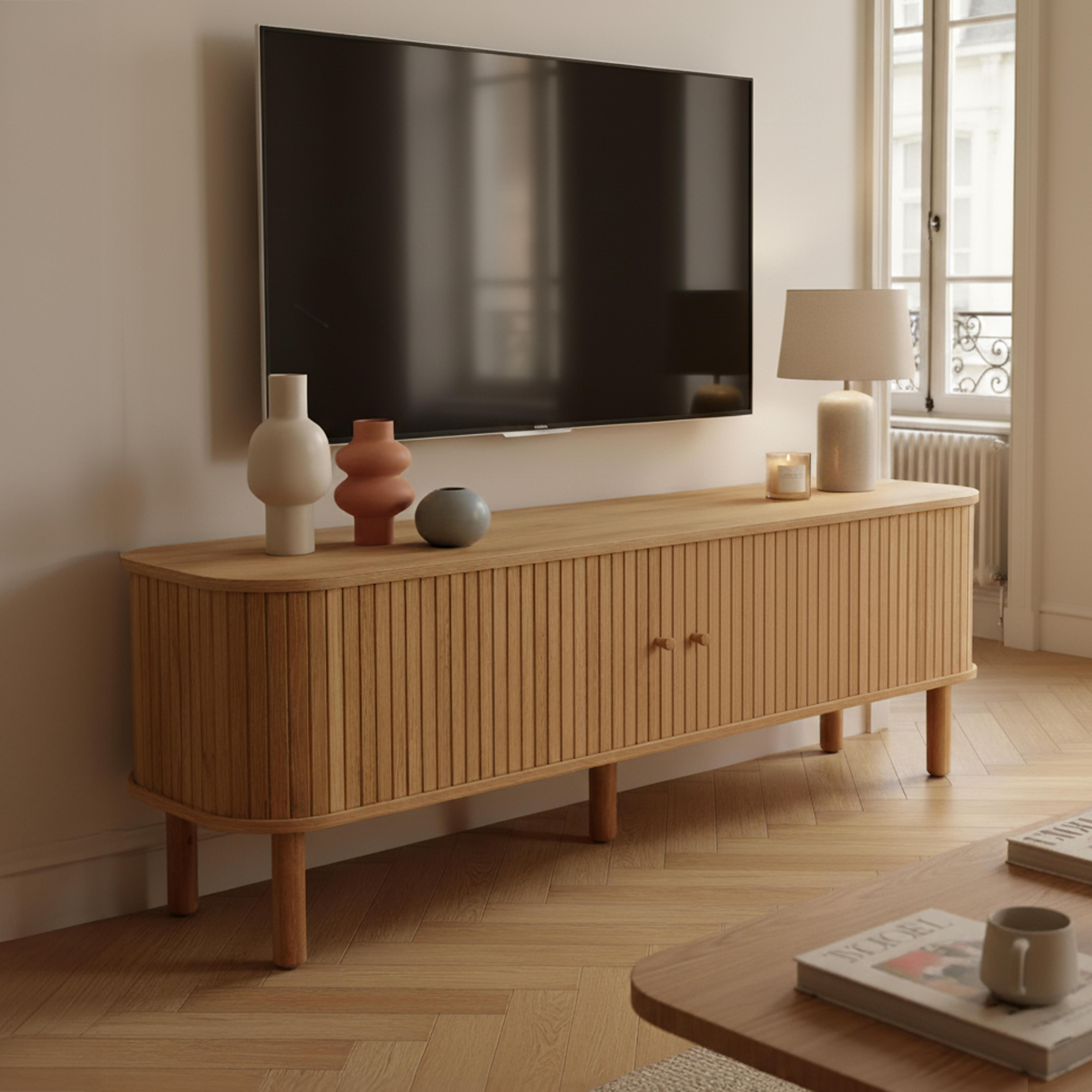 Ein modernes Wohnzimmer mit Fernseher, Holzschrank, Vasen, Lampe und Couchtisch mit Büchern und einer Tasse.