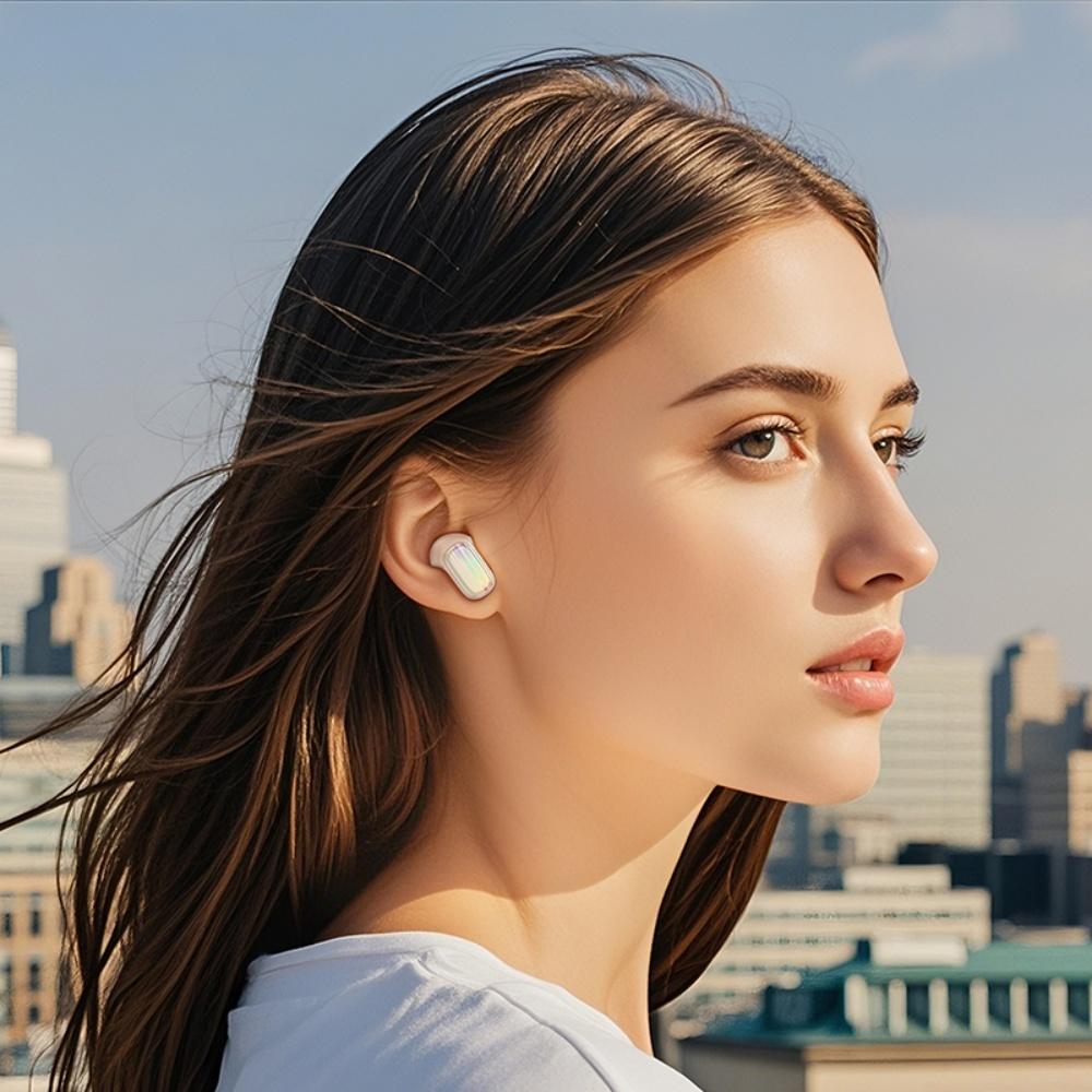 Una mujer con cabello castaño largo, camisa blanca y auricular. Edificios de la ciudad en el fondo, cielo azul.
