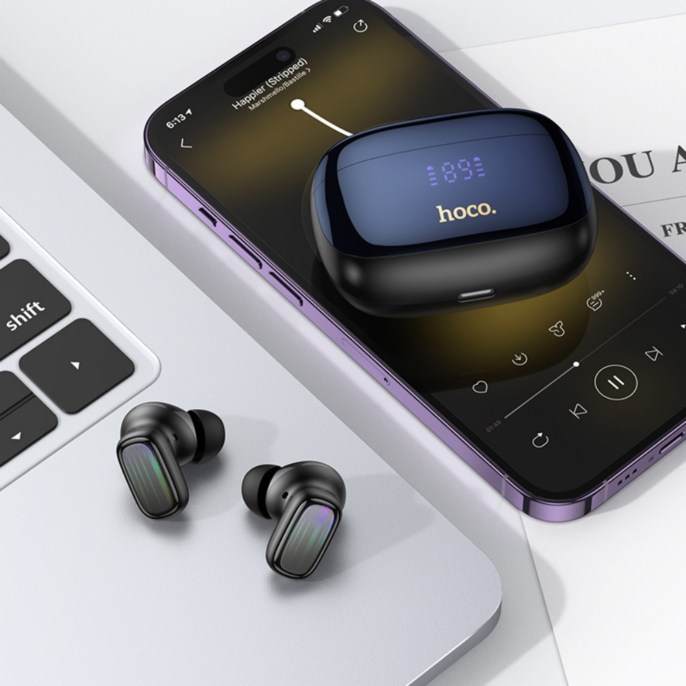 La imagen muestra auriculares inalámbricos negros y su estuche en un teléfono. El teléfono muestra una aplicación de música y un portátil en el fondo.