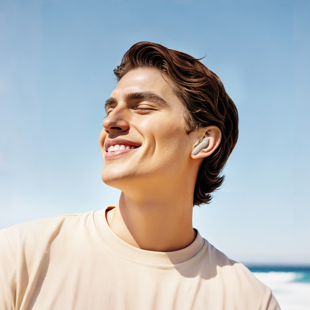 Ein Mann lächelt mit geschlossenen Augen und trägt Ohrhörer. Er ist am Strand mit blauem Himmel und Ozean im Hintergrund.