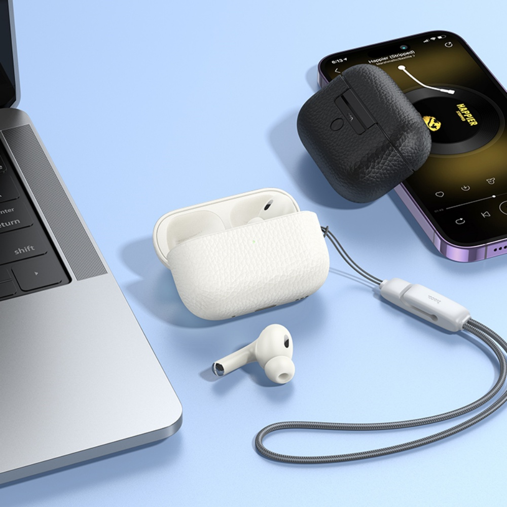 Estuches de auriculares blancos y negros, auriculares y un teléfono están sobre una superficie azul cerca de una laptop. Un cordón conecta los estuches.