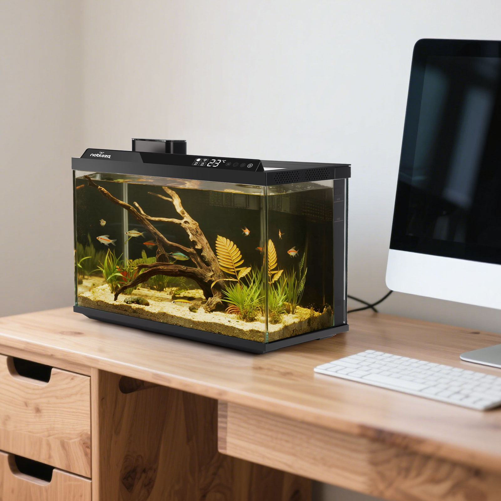 Una pecera con peces, plantas y madera flotante sobre un escritorio de madera. También hay un ordenador y un teclado.