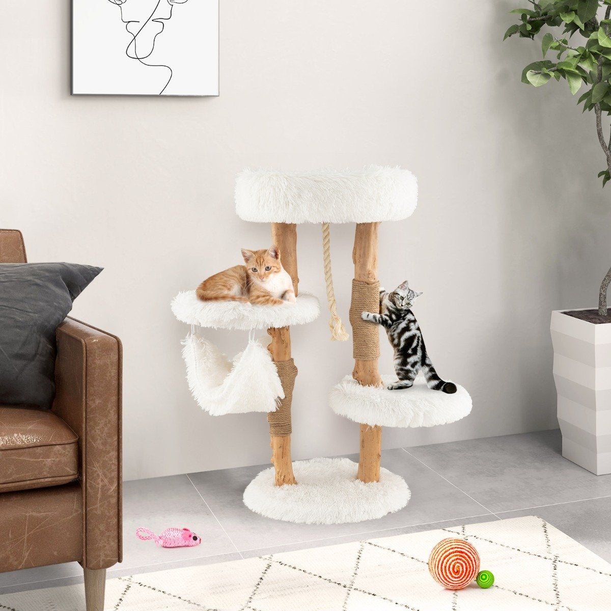 Un árbol para gatos con dos gatos, uno descansando y otro trepando. Un ratón de juguete rosa y una pelota están en el suelo.