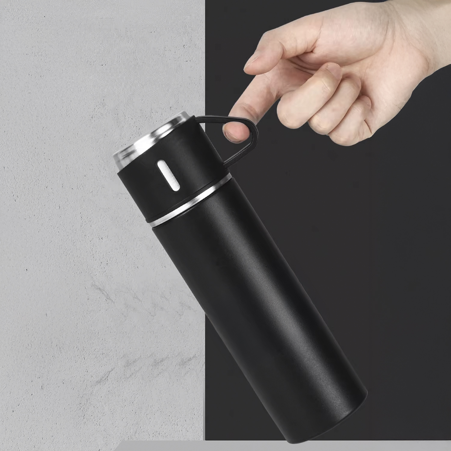Una mano tiene un thermos nero con la parte superiore argentata. Lo sfondo è diviso tra grigio e nero.