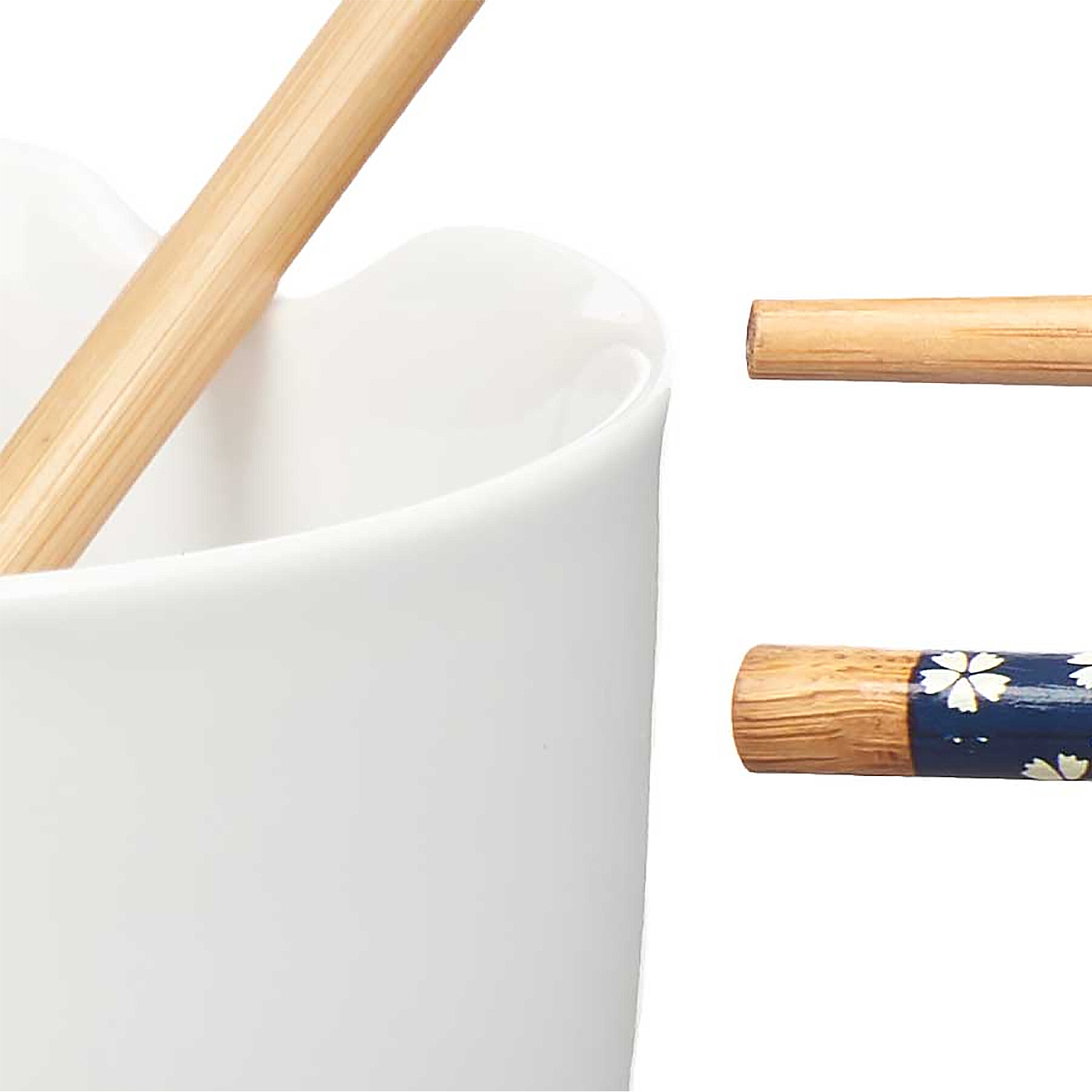 Primo piano di un contenitore in ceramica bianca con due bacchette. Una è in legno naturale, l'altra blu navy con dettagli floreali bianchi.